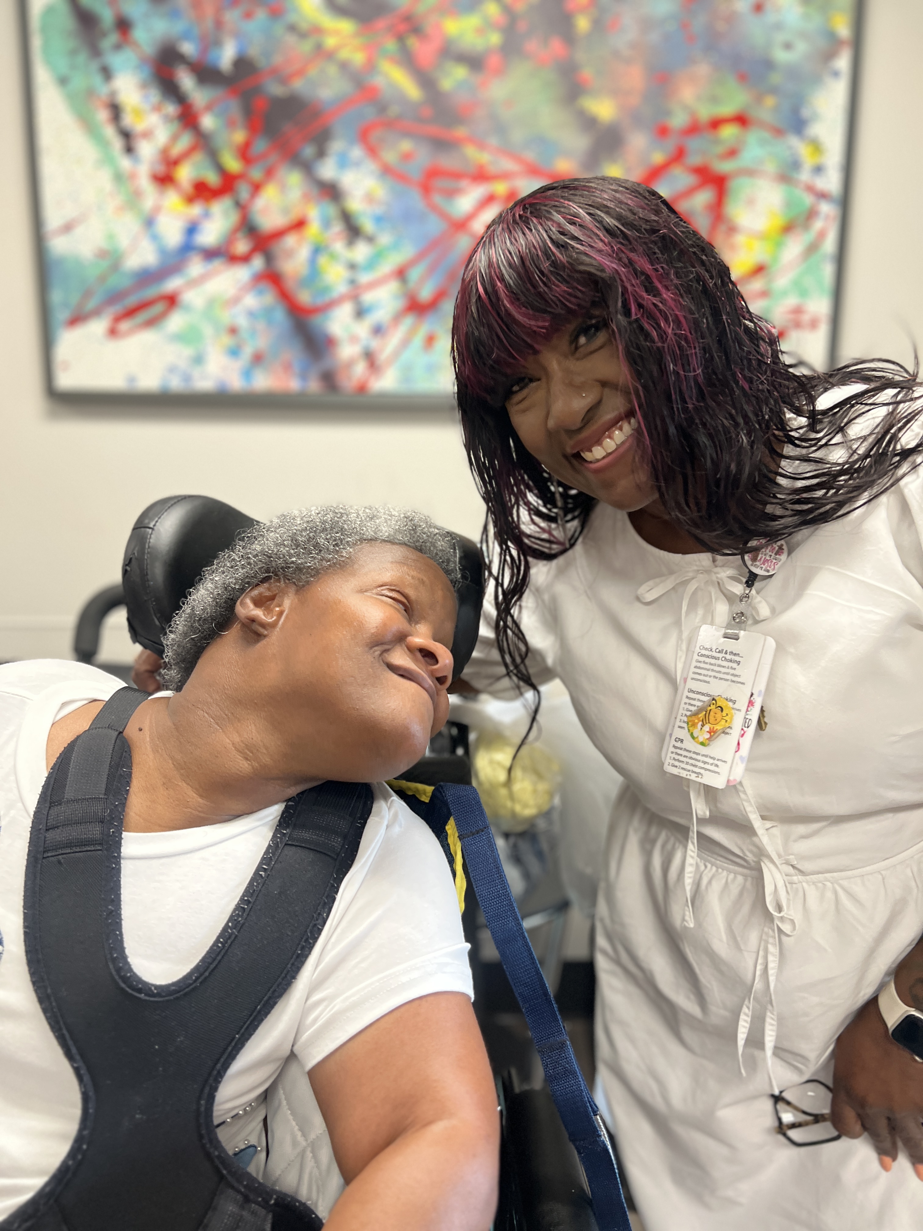 Caregiver and woman in wheelchair smiling together in a supportive care setting, showing compassion and connection.
