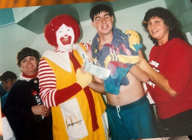 Three people taking a photo with Ronald McDonald in costume.