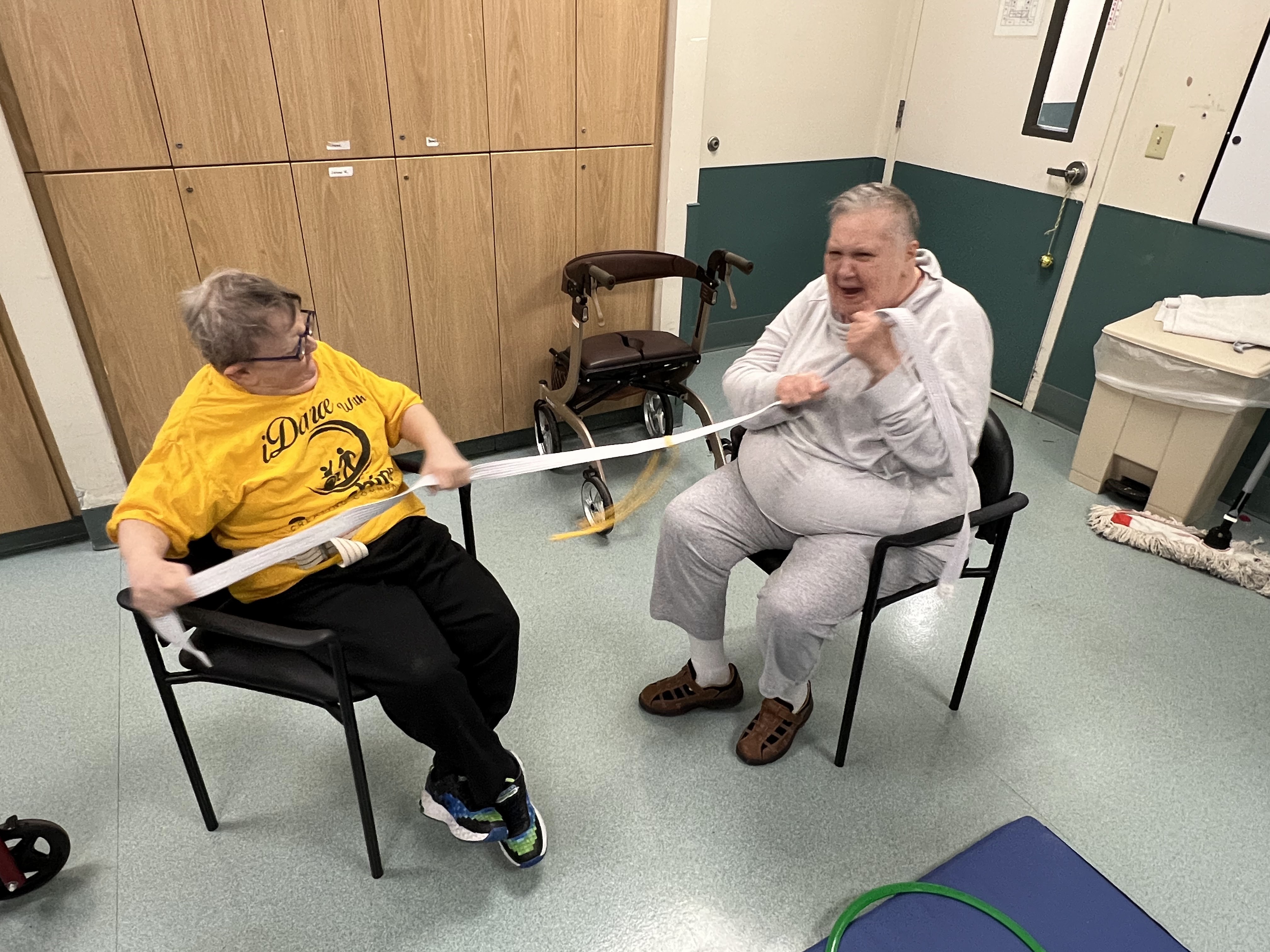Two older adults participate in a seated resistance band workout at Sunshine Communities, demonstrating inclusive fitness activities and active daily living.