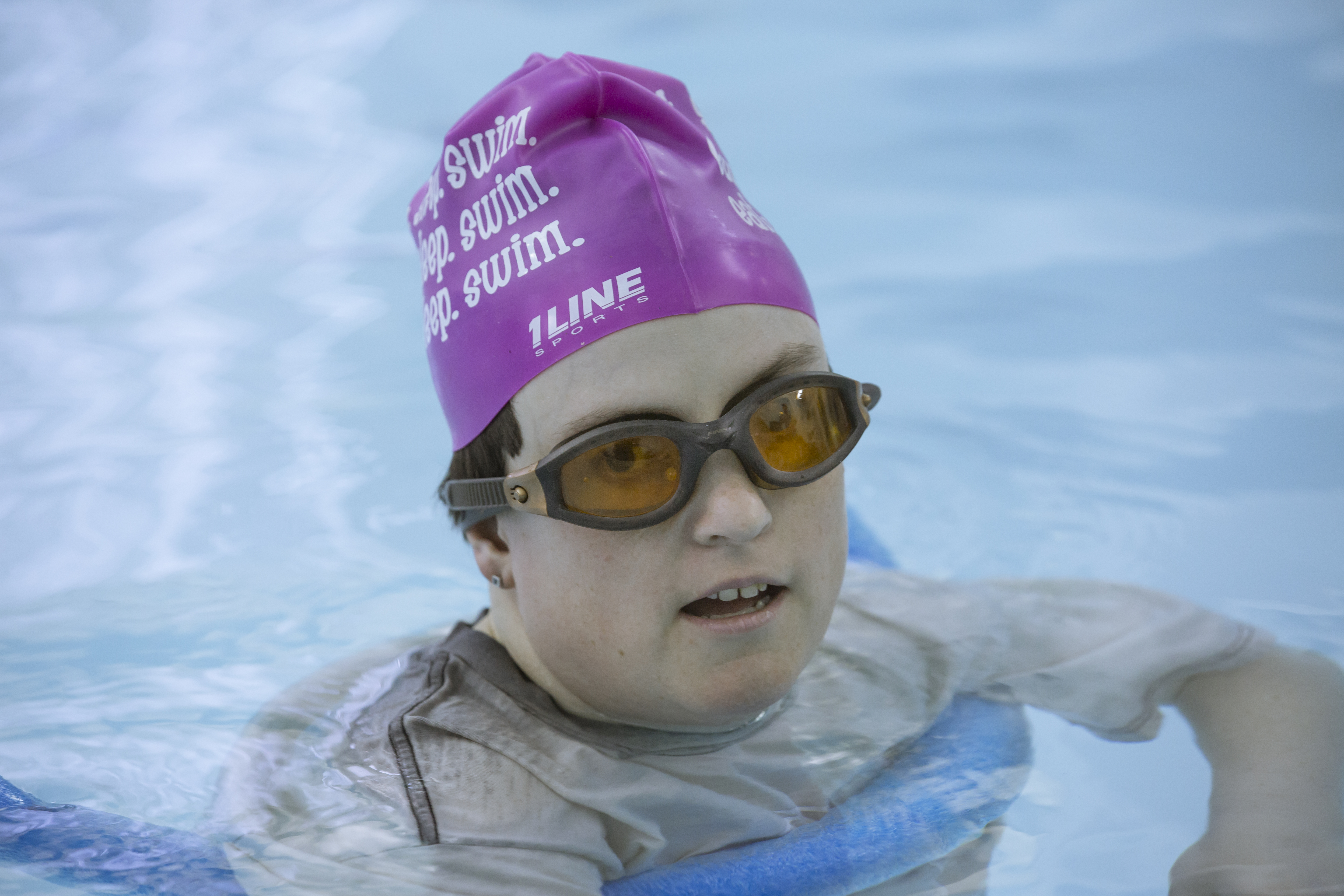Close-up of a woman wearing a pink swim cap and goggles, floating peacefully in Sunshine’s heated therapeutic pool during aquatic therapy.