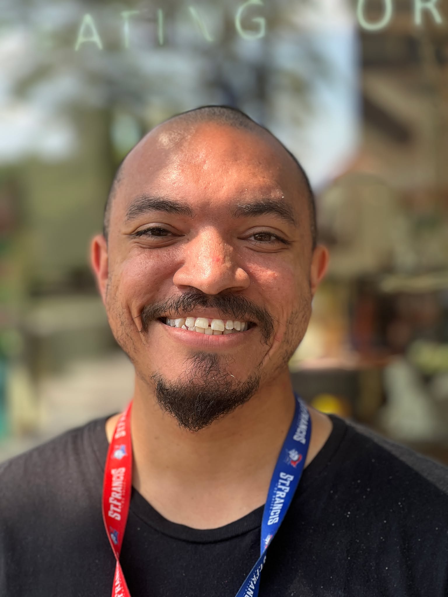 Smiling man wearing a black shirt and lanyard standing outside in sunny weather near Sunshine Communities in Maumee, Ohio.