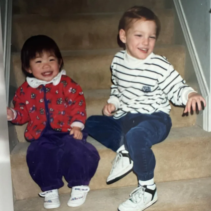 Two young children sit side by side on stairs.