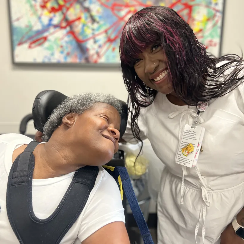 Caregiver and woman in wheelchair smiling together in a supportive care setting, showing compassion and connection.
